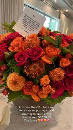 a vase filled with orange and red flowers next to a thank card on top of a table