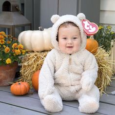 a baby in a teddy bear costume sitting on a porch with pumpkins and hay