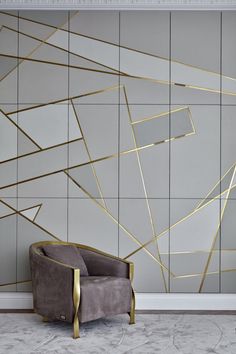 a chair sitting in front of a wall that has gold lines on it and is next to a gray chair