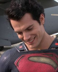 a man in a superman t - shirt standing next to an airplane