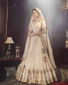 a woman in a white and gold bridal gown standing next to a table with lamps