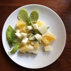 a white plate topped with cut up fruit on top of a wooden table next to a knife and fork