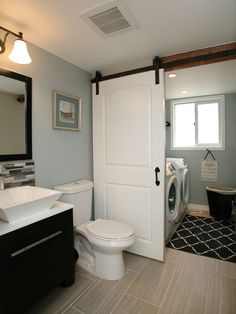 a white toilet sitting next to a sink in a bathroom under a mirror and light