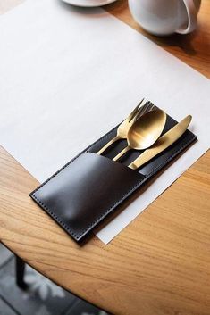 a place setting with two forks and spoons on top of a wooden table next to coffee cups