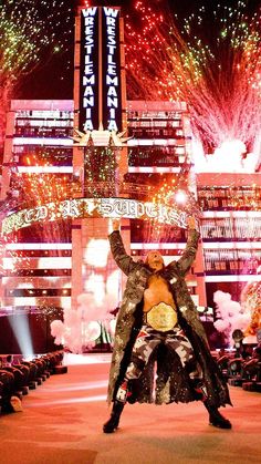 a man standing on top of a stage with his arms in the air and fireworks behind him