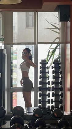 a woman standing in front of a window next to a bunch of dumbbells