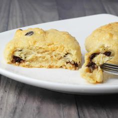 a white plate topped with two scones covered in raisins next to a fork