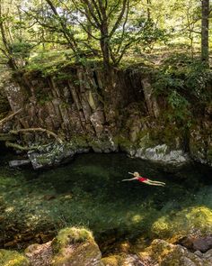 a person in a red kayak is floating on the water near some rocks and trees