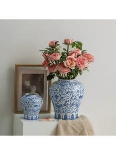 two blue and white vases with pink flowers in them sitting on a table next to a framed photograph