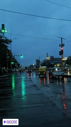 cars are driving down the street in the rain at night with green traffic lights on