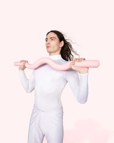 a man holding a pink object in his hands while standing against a pink background with long hair