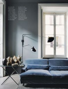 a blue couch sitting in front of a window next to a table with vases on it