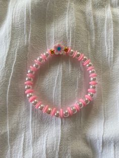 a pink beaded bracelet with flowers and pearls on top of a white cloth covered bed