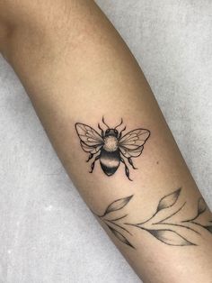 a black and white photo of a bee tattoo on the left arm with leaves around it