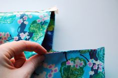 someone is sewing something on the side of a blue flowered bag with green and pink flowers