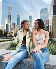 two women sitting on a ledge in front of the city