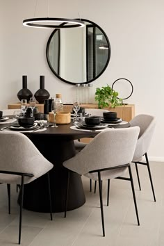 a round dining table with chairs around it and a circular mirror hanging above the table