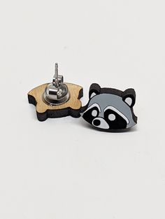 a raccoon pin sitting on top of a piece of wood next to a metal object