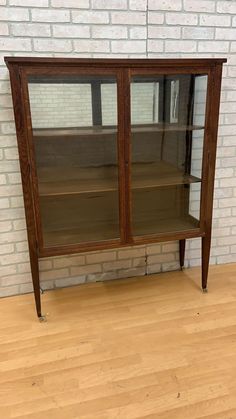 a wooden cabinet sitting on top of a hard wood floor next to a brick wall