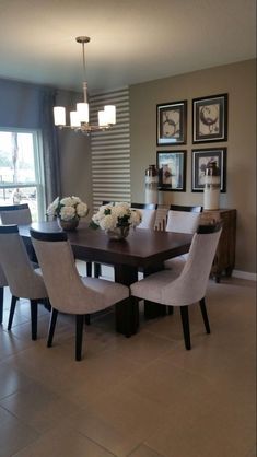 a dining room table with chairs and pictures on the wall in front of it's windows