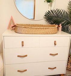 a white dresser with a basket on top of it and a mirror in the background