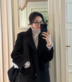 a woman taking a selfie in front of a mirror wearing a coat and sweater