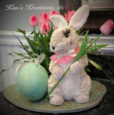 a white stuffed rabbit sitting on top of a table next to pink tulips