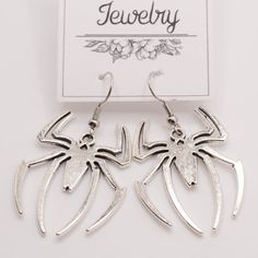 pair of spiderman earrings in silver tone on white background with jewelry tag attached to it