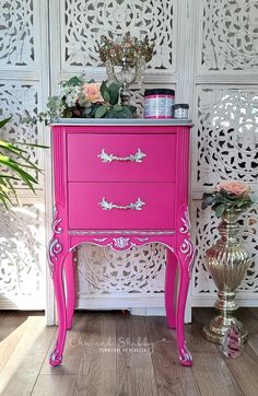 a pink dresser sitting next to a vase with flowers on it and a white wall behind it