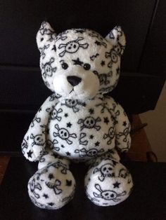 a white teddy bear with skulls and stars on it's chest sitting in front of a television