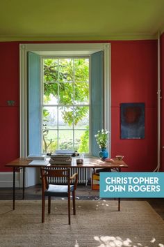 a dining room with red walls and wooden table in the foreground is an open window