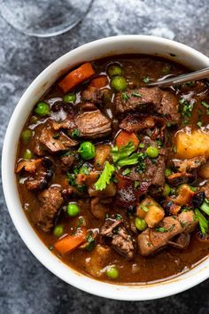 a bowl of beef stew with carrots, peas and potatoes on a gray surface