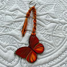 a butterfly keychain is sitting on a white doily with an orange tassel