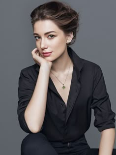 a woman sitting down with her hand on her chin and looking at the camera while wearing a black shirt