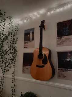 an acoustic guitar is hanging on the wall next to some plants and pictures with lights