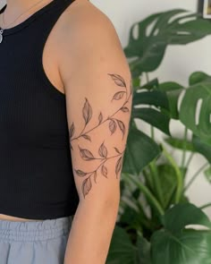 a woman with a tattoo on her arm is standing in front of a potted plant