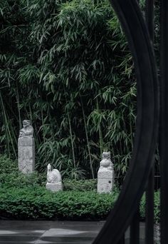 some statues in the middle of a garden with bamboo trees behind them and an iron gate