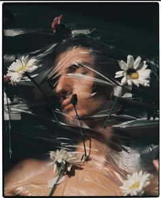 a woman is wrapped in plastic with flowers on her head and nose, looking at the camera