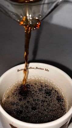 coffee being poured into a white cup on top of a saucer with black stuff in it