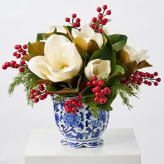 a blue and white vase with red berries, flowers and greenery in it sitting on a table