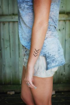 a woman's arm with a small arrow tattoo on her left side, and the word