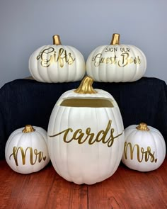 three white pumpkins with gold lettering on them