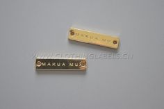 two gold metal name tags on a gray surface with the words manua muna written below them