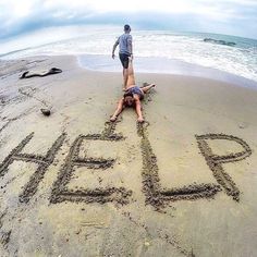 a person laying on top of a sandy beach next to the words help written in sand