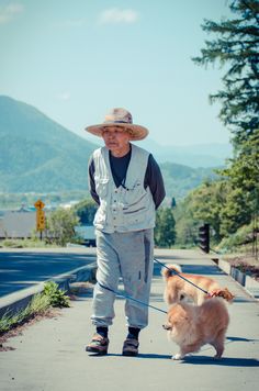 an old man walking his dog on a leash down the street with mountains in the background