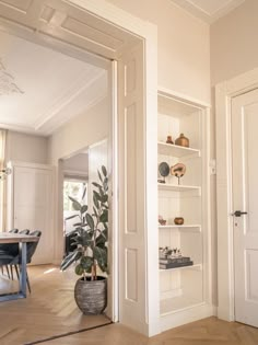 an open door leading to a dining room with a potted plant in the corner