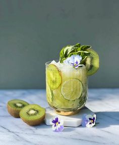 a glass filled with cucumber, kiwi and flowers on top of a table