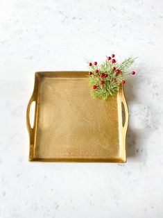 a gold tray with red berries and greenery in it on a marble countertop