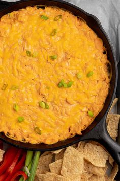 a skillet filled with cheesy dip surrounded by vegetables and tortilla chips