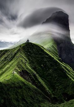 a large green mountain covered in fog and mist next to the ocean on a cloudy day